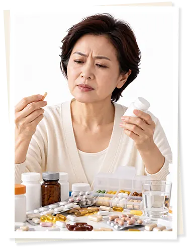 中年女士皱眉看着手中的药片,桌上堆满药瓶和药盒
