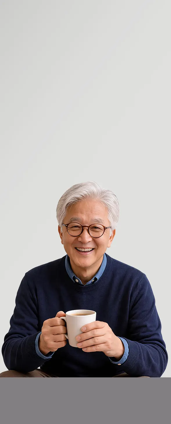 A silver-haired older person in round glasses and a dark blue jumper holds a mug in both hands, smiling happily