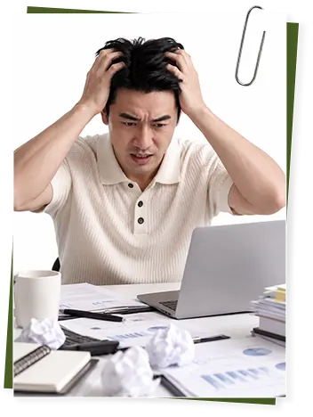男士双手抱头,面对笔记本电脑和一桌文件显得疲惫焦虑